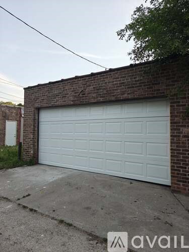 A white garage door is closed and the wall is made of bricks.