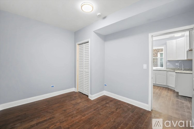 A room with wooden floors and a white door leading to a kitchen.