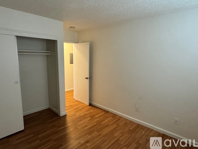 A room with wooden floors and white walls, with a doorway leading to another room.