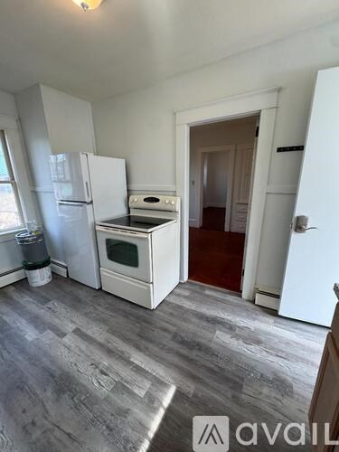 A kitchen with a white fridge and oven, a grey floor, and a doorway leading to another room.
