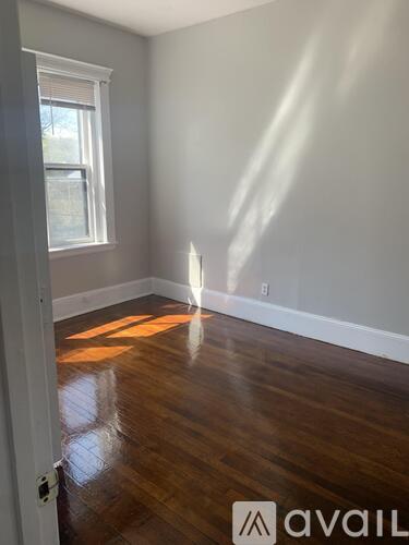 A room with wooden floors and a window letting in sunlight.