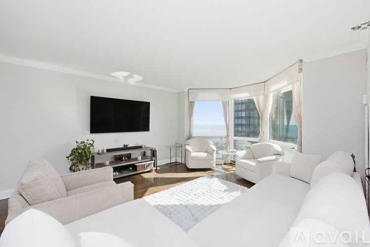 A living room with a flat screen TV, white sofa, and a large window with a view of a building outside.