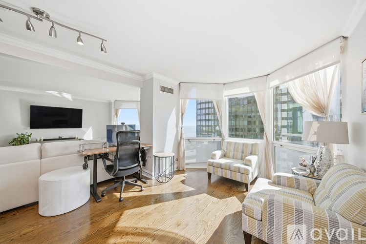 A living room with a television, a desk, a chair, a couch, and a window with curtains.