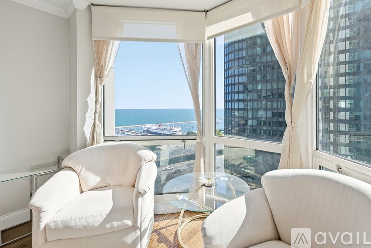 Two white chairs are placed in front of a window with a view of the city and the sea.
