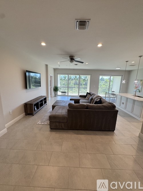 A spacious living room with a brown couch and a flat screen TV mounted on the wall.
