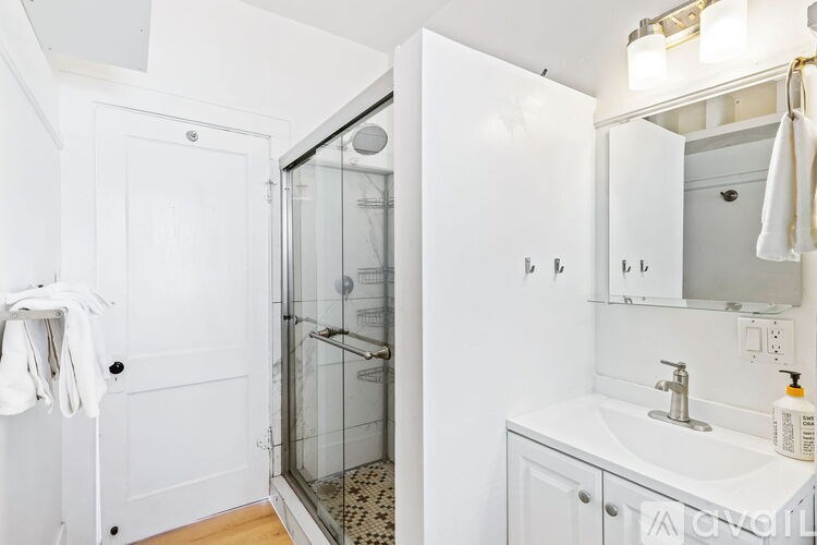 A white bathroom with a glass shower door and a white sink.
