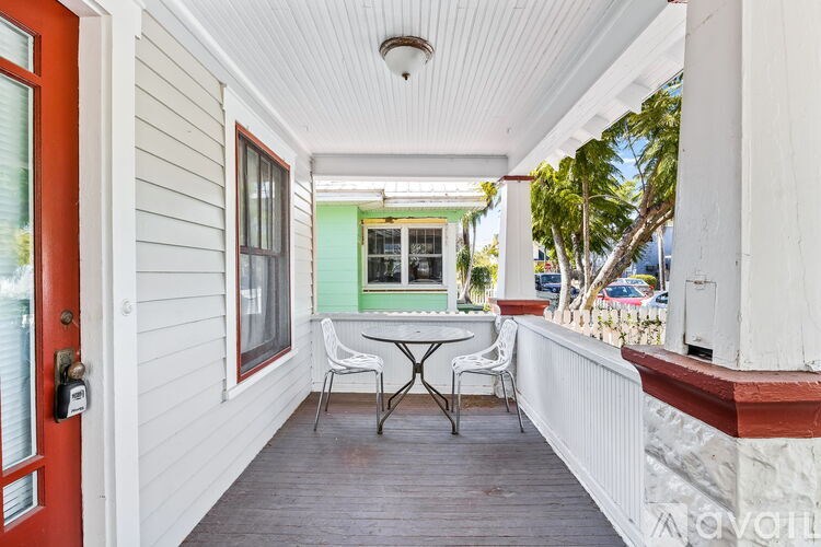 A white porch with a red door and a table and chairs.