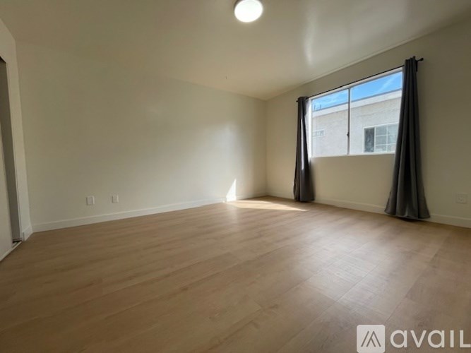 A spacious room with wooden flooring and a window with curtains.