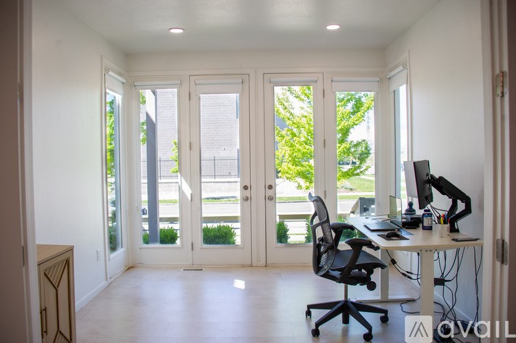 A room with a desk and a computer with a window in the background.