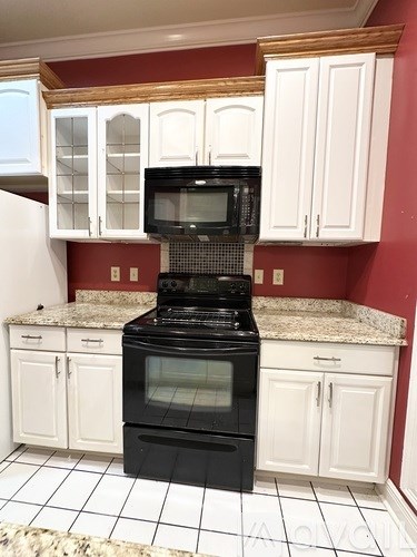 A black stove top oven with a microwave on top is in a kitchen with white cabinets.