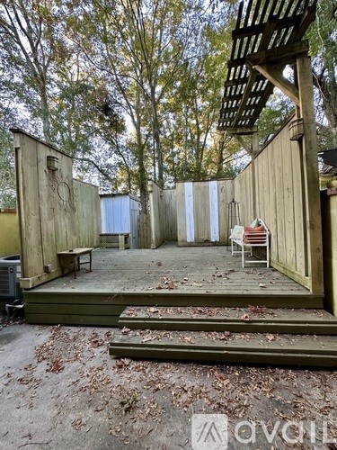 A wooden deck with a bench and a chair is surrounded by trees.