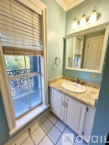 A bathroom with a sink, mirror, and window with blinds.