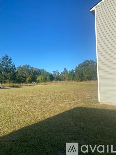 A grassy field with a house and trees in the background.