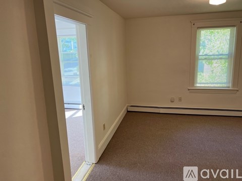 A room with a carpeted floor, a window with blinds, and a door leading to a hallway.
