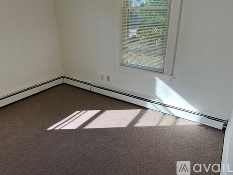 A room with a carpeted floor and a window letting in sunlight.