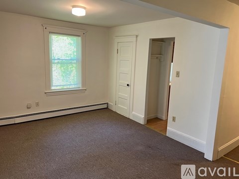 A room with a carpeted floor, a window with blinds, a door, and a wall-mounted light fixture.