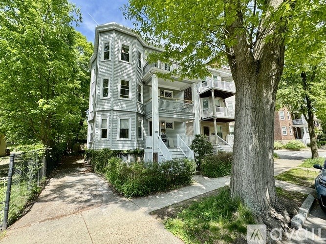 A large, old building with a grey facade is surrounded by green trees.