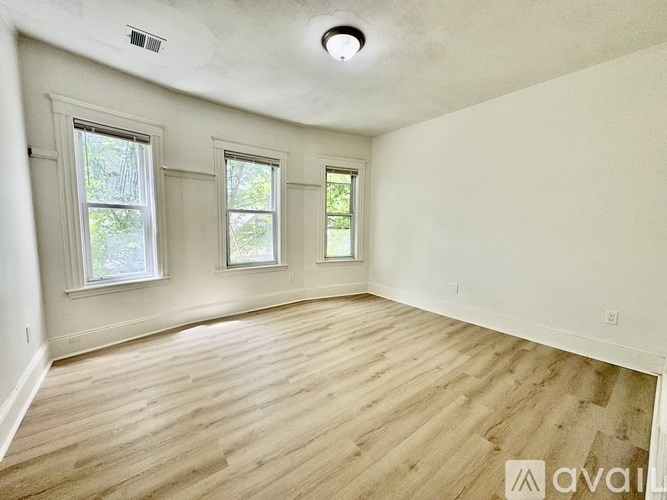 A room with wooden flooring and three windows.