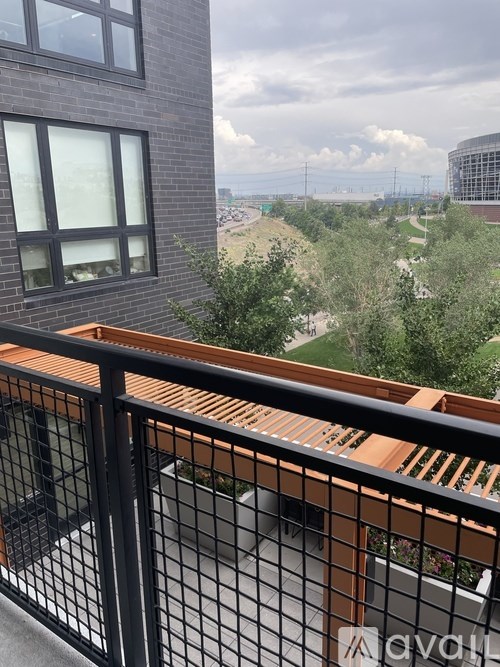 A balcony with a black railing and a view of a green landscape and buildings in the distance.