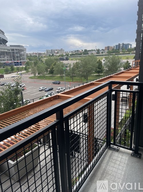 A balcony with a black railing and a view of a parking lot and buildings.