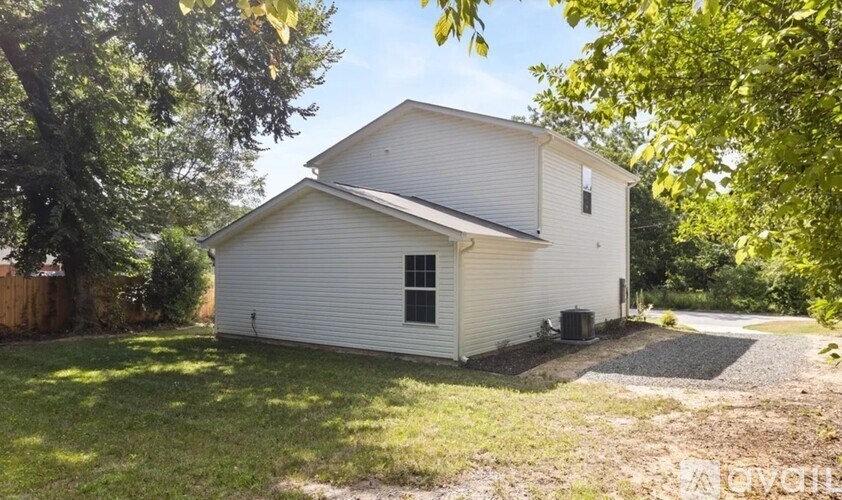 A white house with a black door is surrounded by greenery.