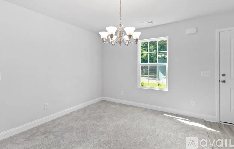 A room with a chandelier, carpeted floor, and a window showing greenery outside.