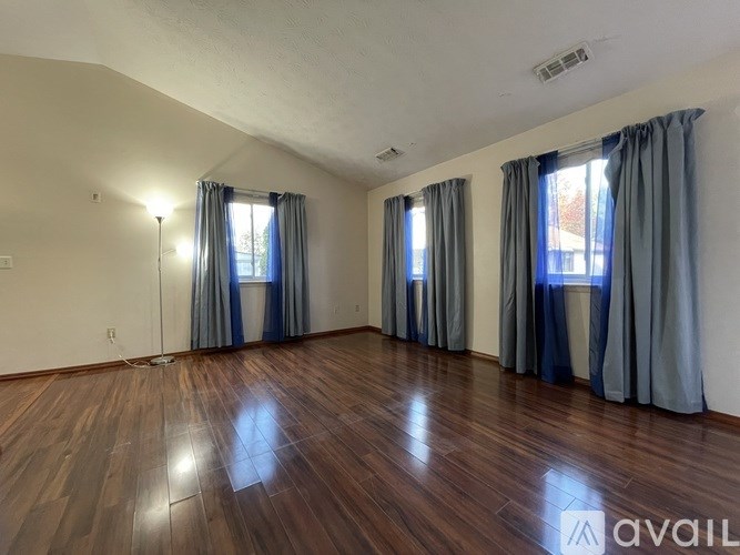 A room with wooden floors and two windows with curtains.