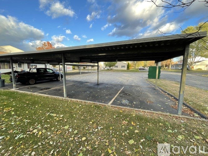 A parking lot with a black car and a green trash can under a metal roof.