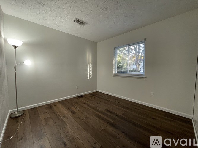 A room with wooden flooring and a window with blinds.