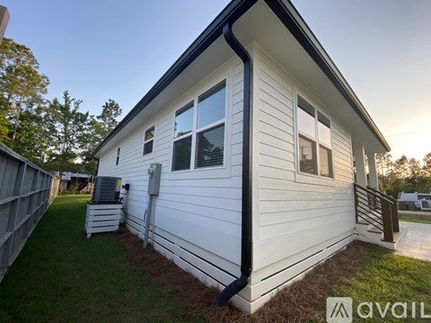 A small white house with a black roof and a brown fence.