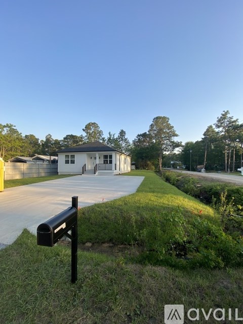 A small white building with a black roof is surrounded by greenery and a mailbox is in the foreground.