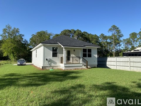 A small white house with a black roof is surrounded by a grassy lawn.