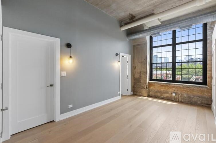 A room with a large window and wooden floors is available for rent.