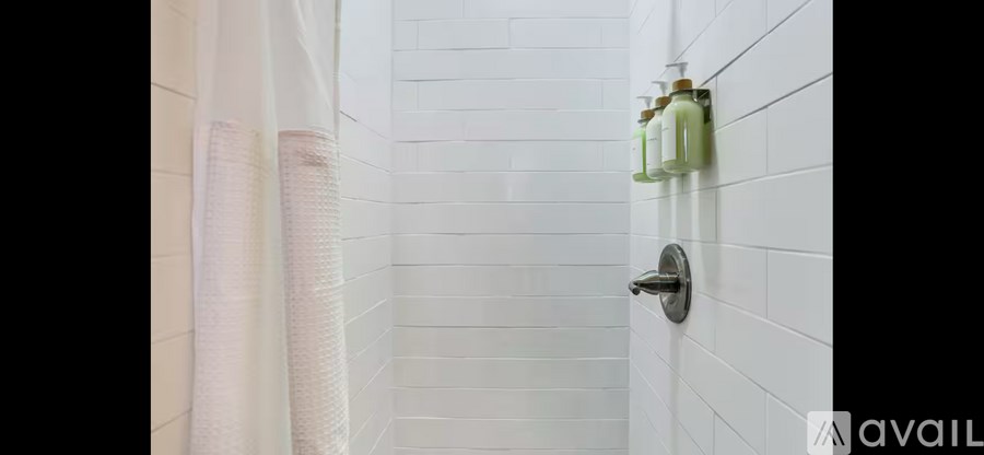 A white tiled bathroom with a shower curtain and a shower head.