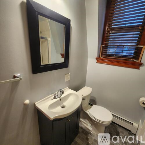 A bathroom with a toilet, sink, mirror, and window.