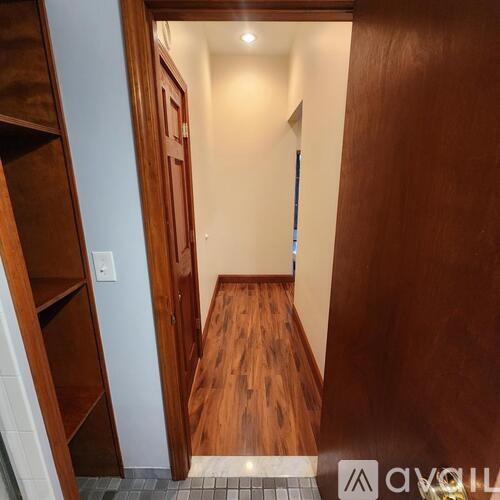A hallway with a wooden floor and a door on the left.