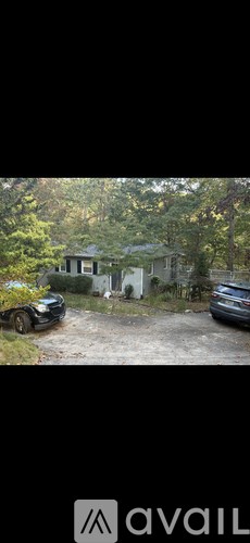 A car is parked in front of a house surrounded by trees.