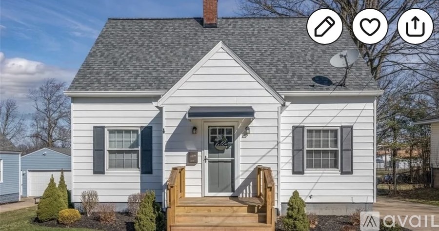 A small white house with a grey roof and a wooden deck in front.
