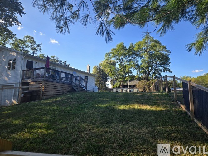 A house with a white exterior and a balcony is surrounded by a grassy area and trees.