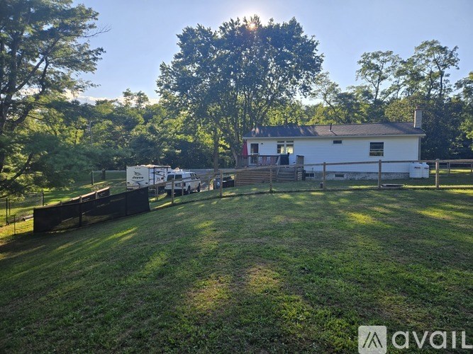 A white house with a black roof is surrounded by a grassy field and trees.