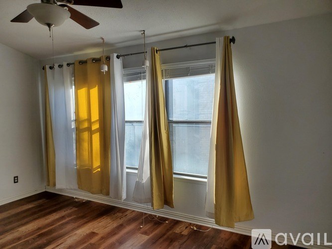 A room with a ceiling fan and a window with yellow curtains.