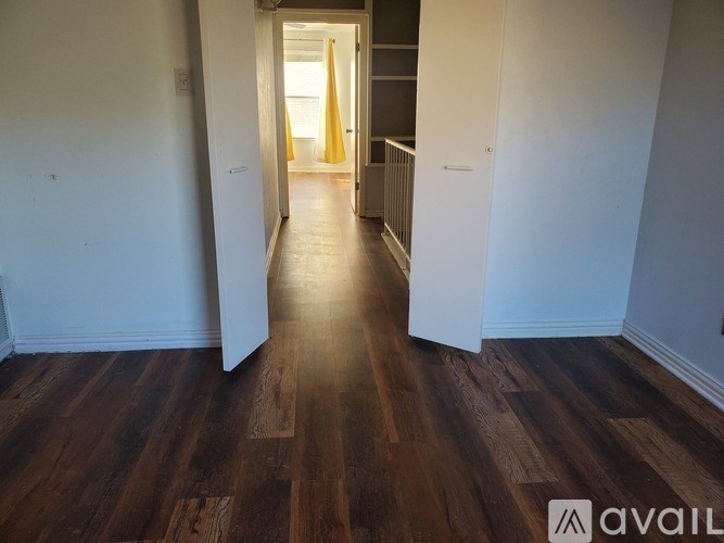 A hallway with wooden floors and white walls leading to a door.