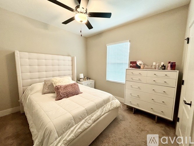 A bedroom with a white bed and a white dresser with a window.