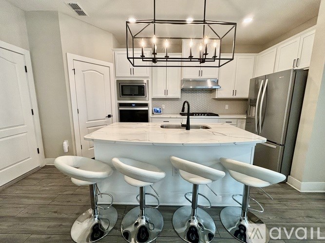 A kitchen with white cabinets and a white island with three stools.