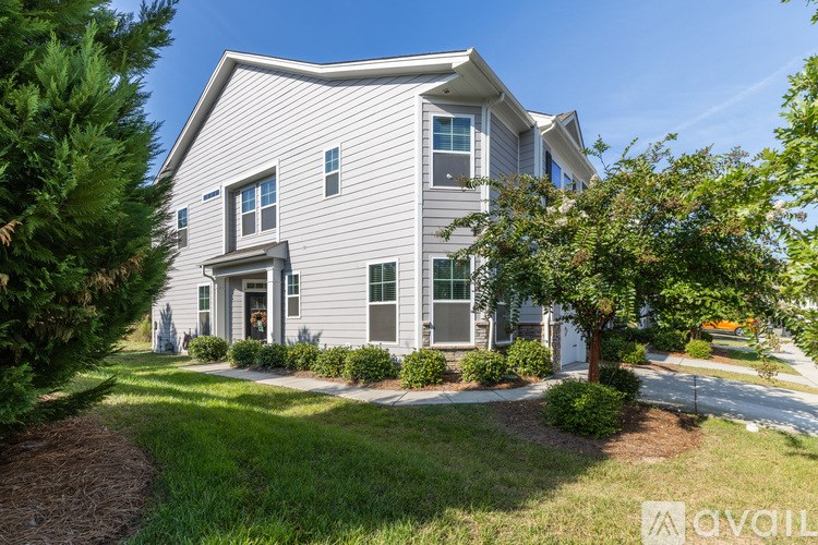 A house with a grey siding and a white door is surrounded by greenery.
