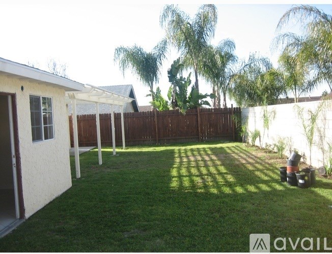 A backyard with a white house, green grass, and trees.