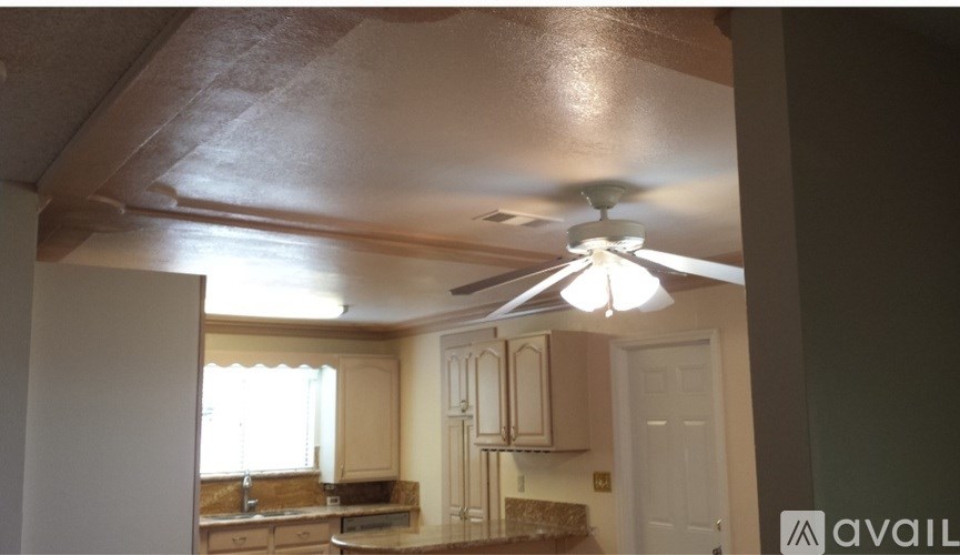 A kitchen with a fan on the ceiling and a window with curtains.
