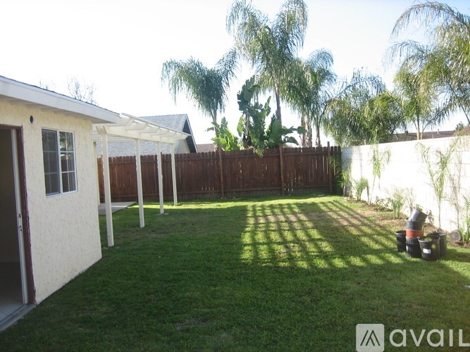 A backyard with a white house, green grass, and trees.