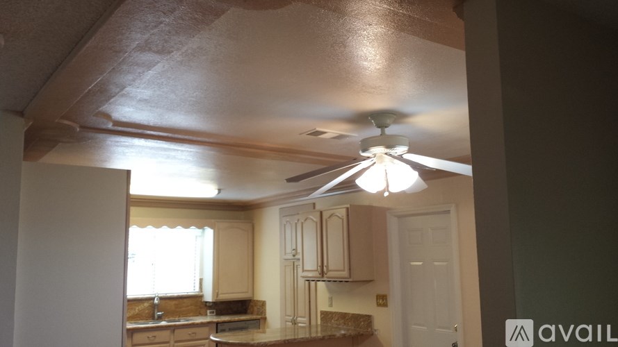 A kitchen with a fan on the ceiling and a window with curtains.