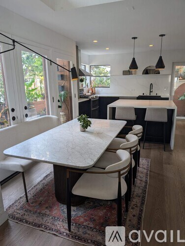 A kitchen with a table and chairs in the foreground and a window with a view of trees in the background.